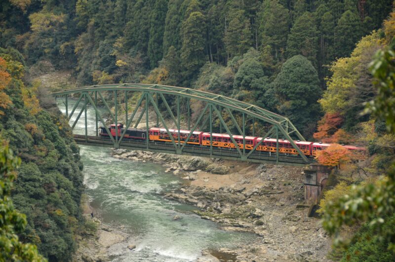 秋の保津峡の鉄橋を渡る嵯峨野トロッコ列車
